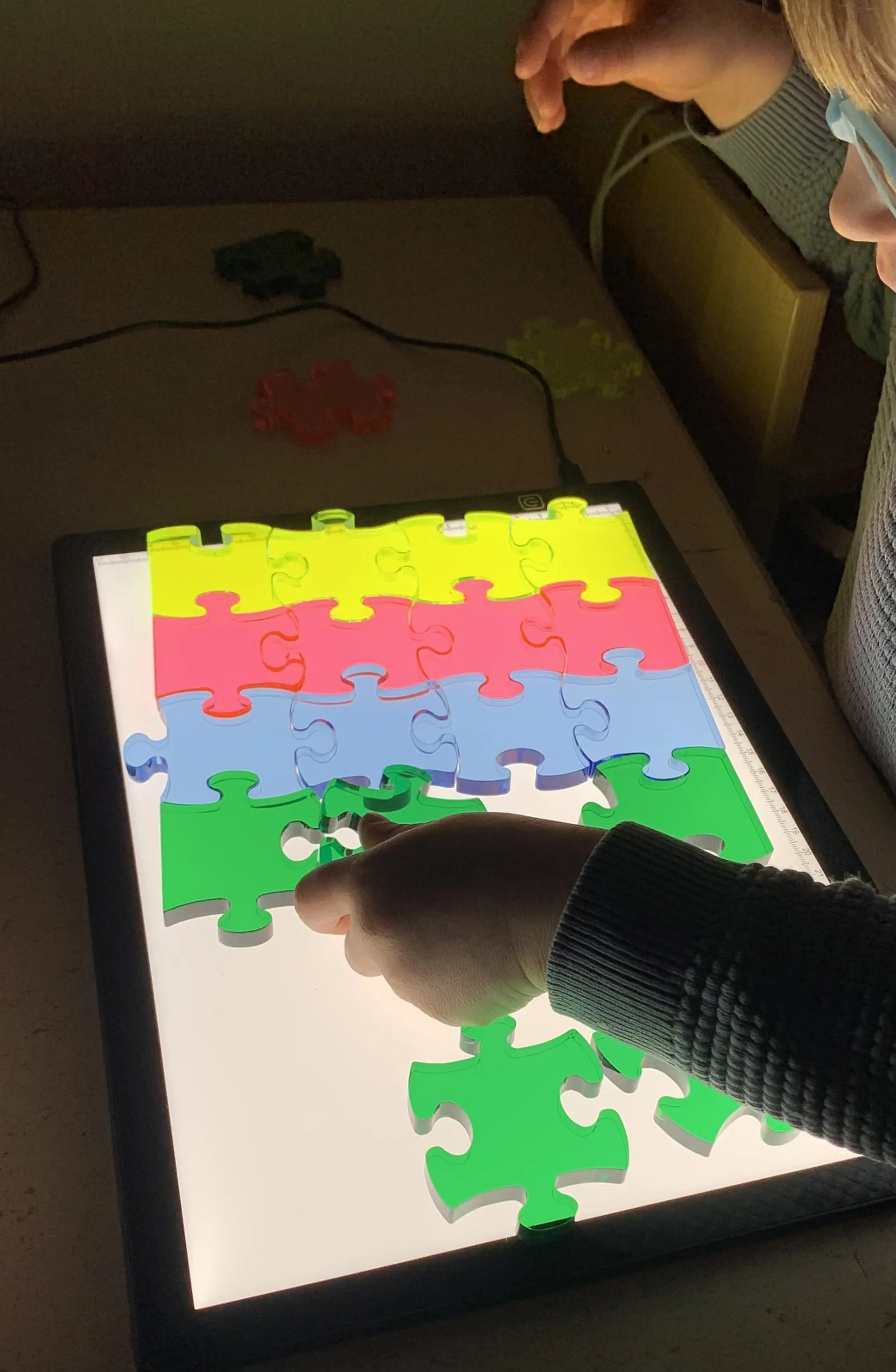 Wahrnehmungsförderung: Kinderhände beim Puzzeln auf einem Leuchttisch mit transparenten, kontrastreichen Formen zur visuellen und taktilen Stimulation in der Frühförderung.
