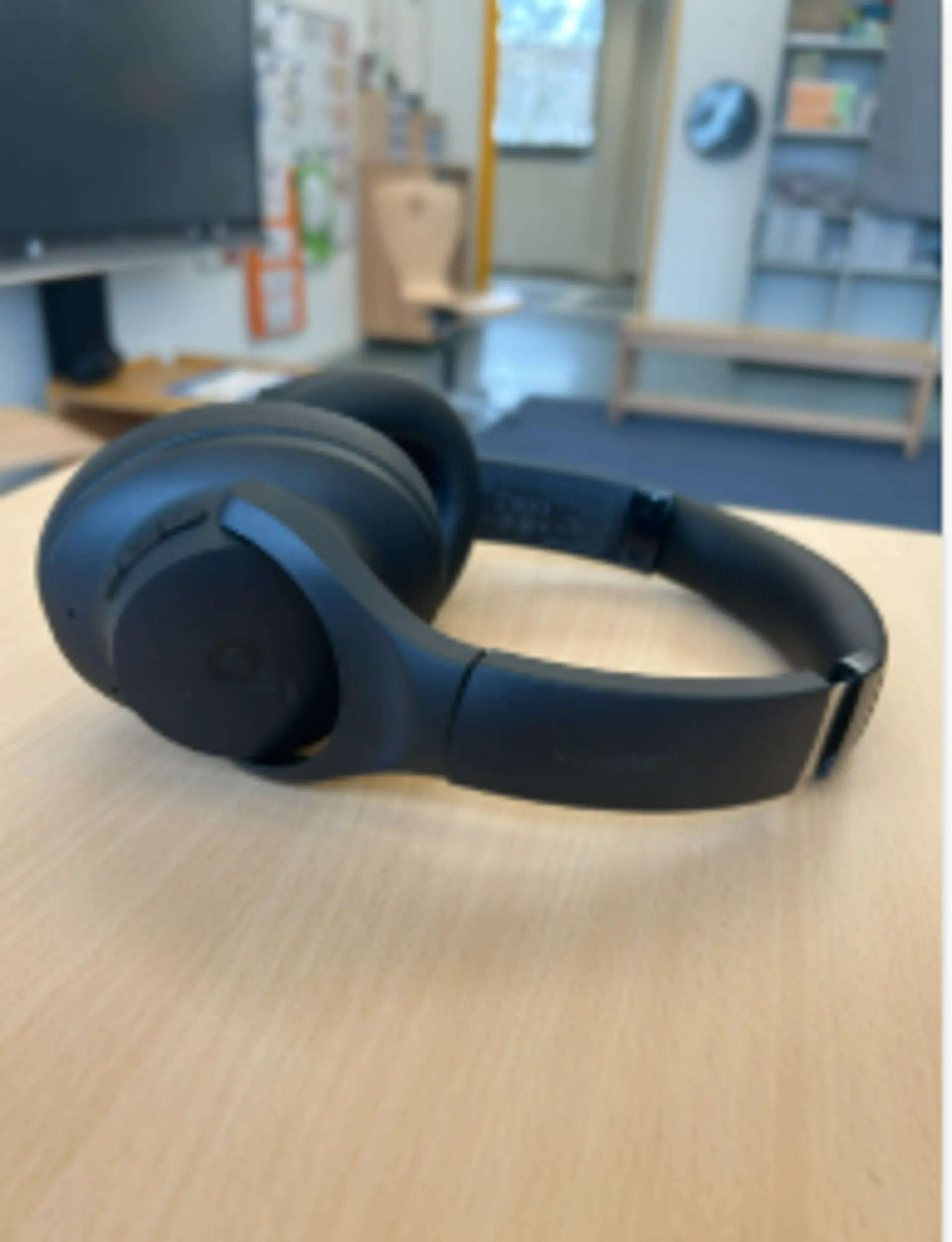 Große, Ohren überdeckende und verstellbare Kopfhörer liegen auf einem Schreibtisch in einem Klassenraum.