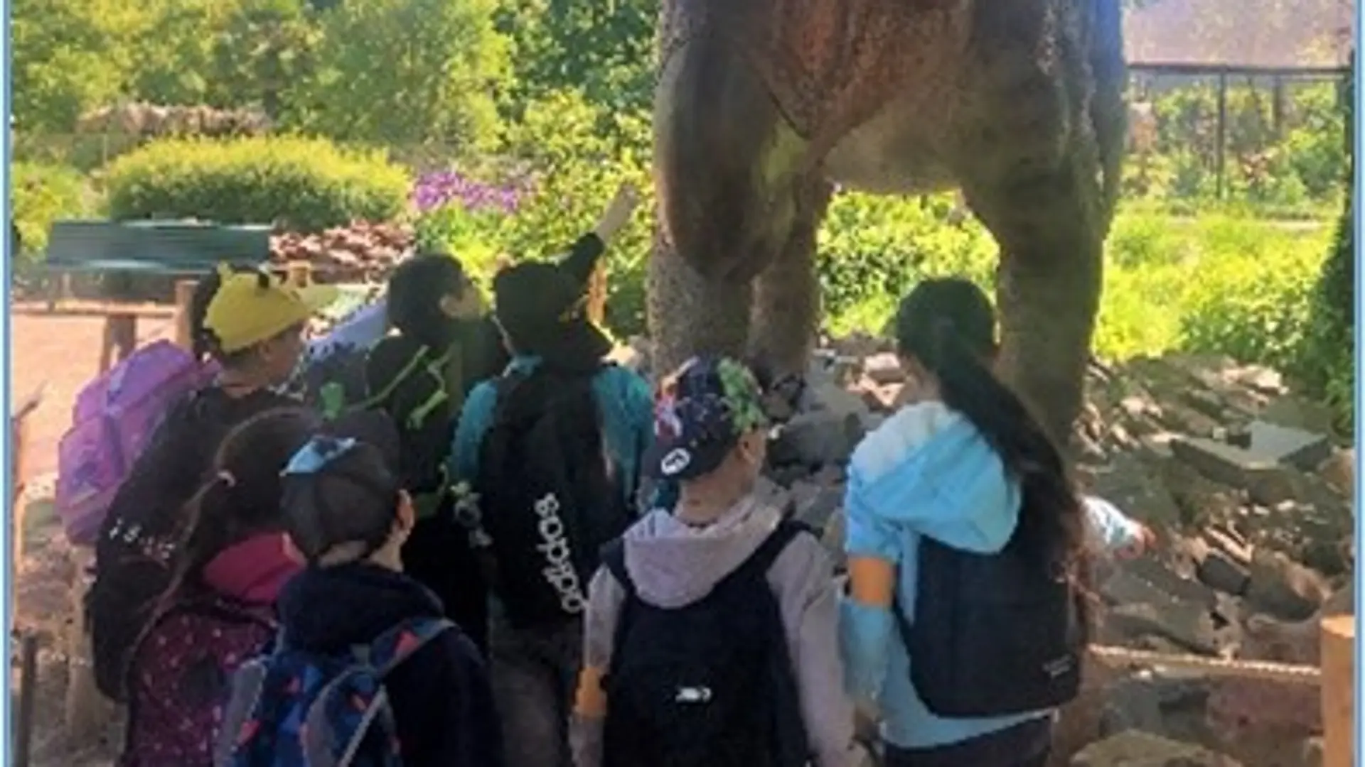 Eine Gruppe aus acht Schüler*innen steht vor einer großen Tierfigur auf dem Zoogelände und betrachtet sie.
