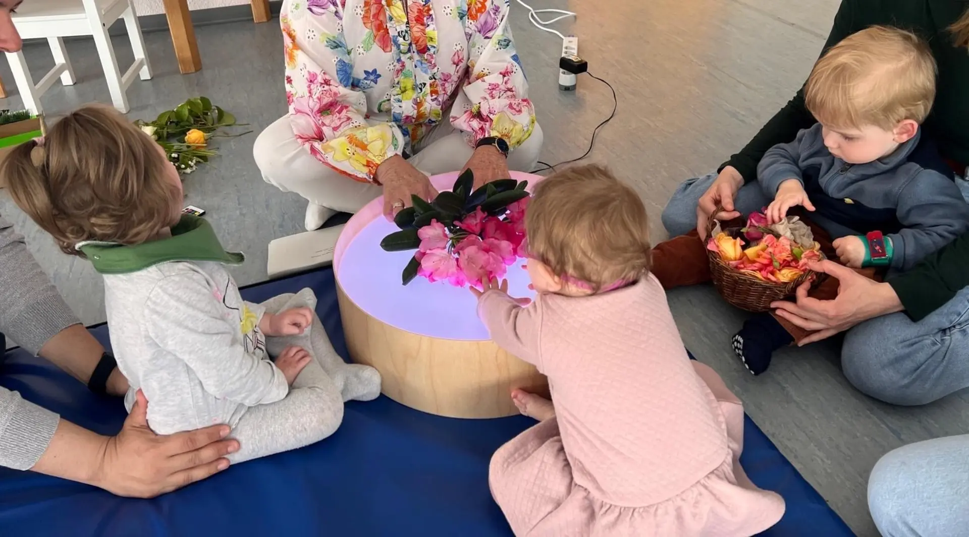 Babys entdecken Frühlingsmaterialien auf einer Leuchttrommel in der Babyspielgruppe