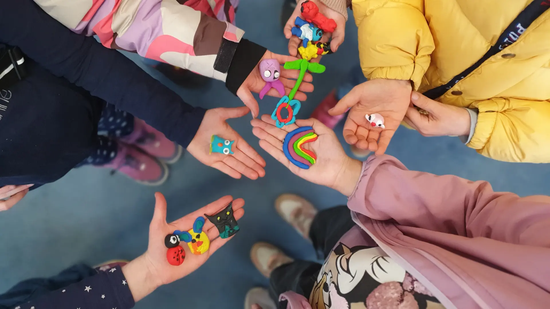 Das Bild zeigt Kinderhände. Sie halten bunte Fimo-Figuren