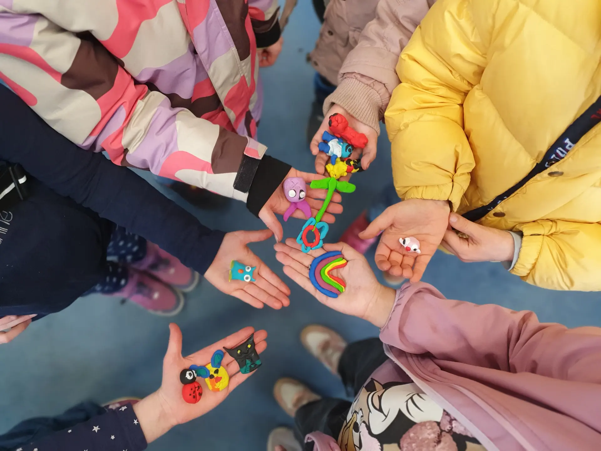 Mehrere Kinderhände von oben fotografiert, die die selbstgebastelten Fimo-Figuren präsentieren.