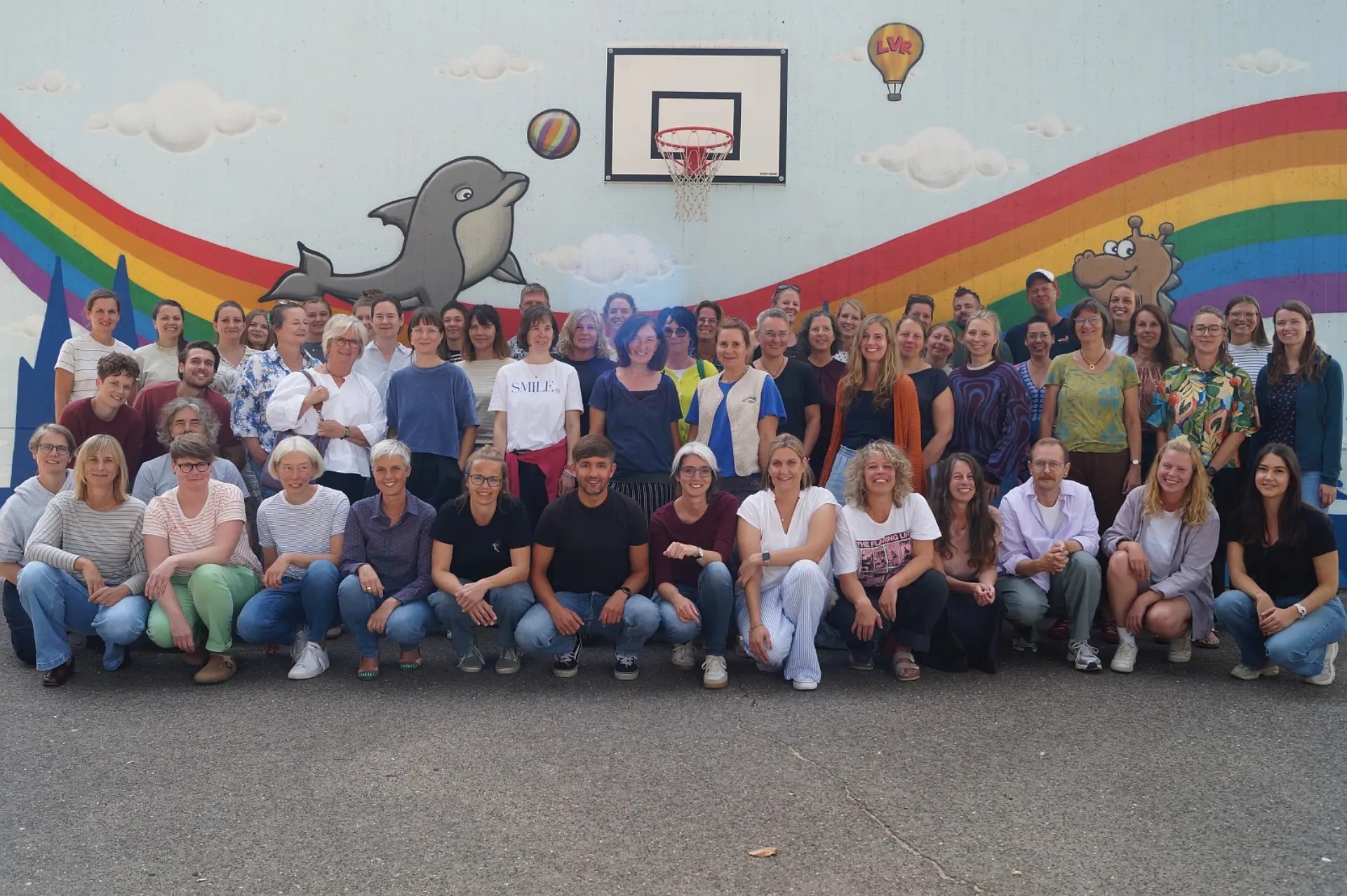 Gruppenporträt des gesamten Kollegiums der LVR-Severin-Schule vor einer bunt bemalten Wand im Schulinnenhof