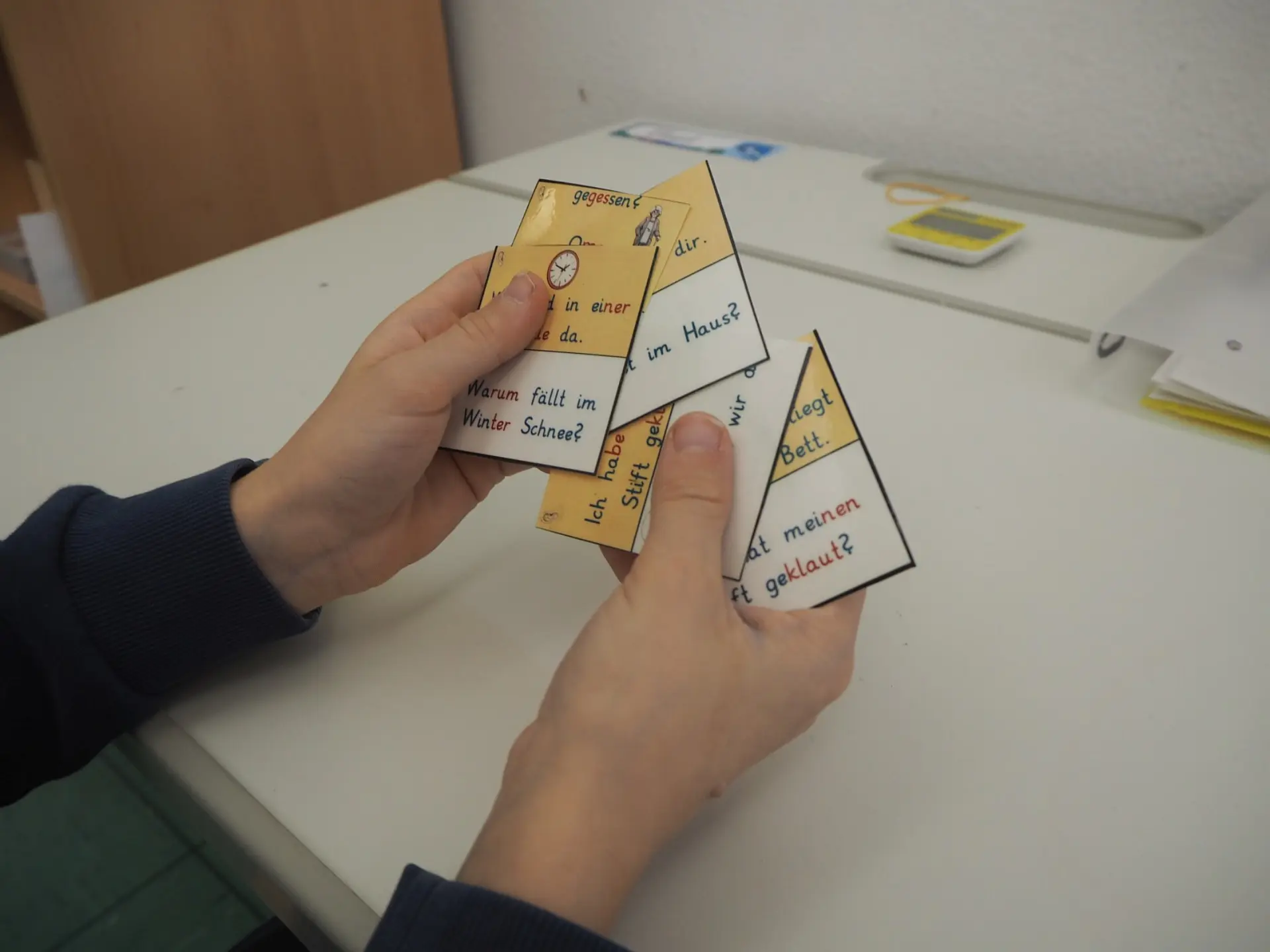 Nahaufnahme von zwei Händen, die mehrere laminierte, viereckige Hilfskarten aus Papier halten. Die Karten sind in deutscher Sprache bedruckt und zeigen Anfänge von Sätzen oder Fragen.