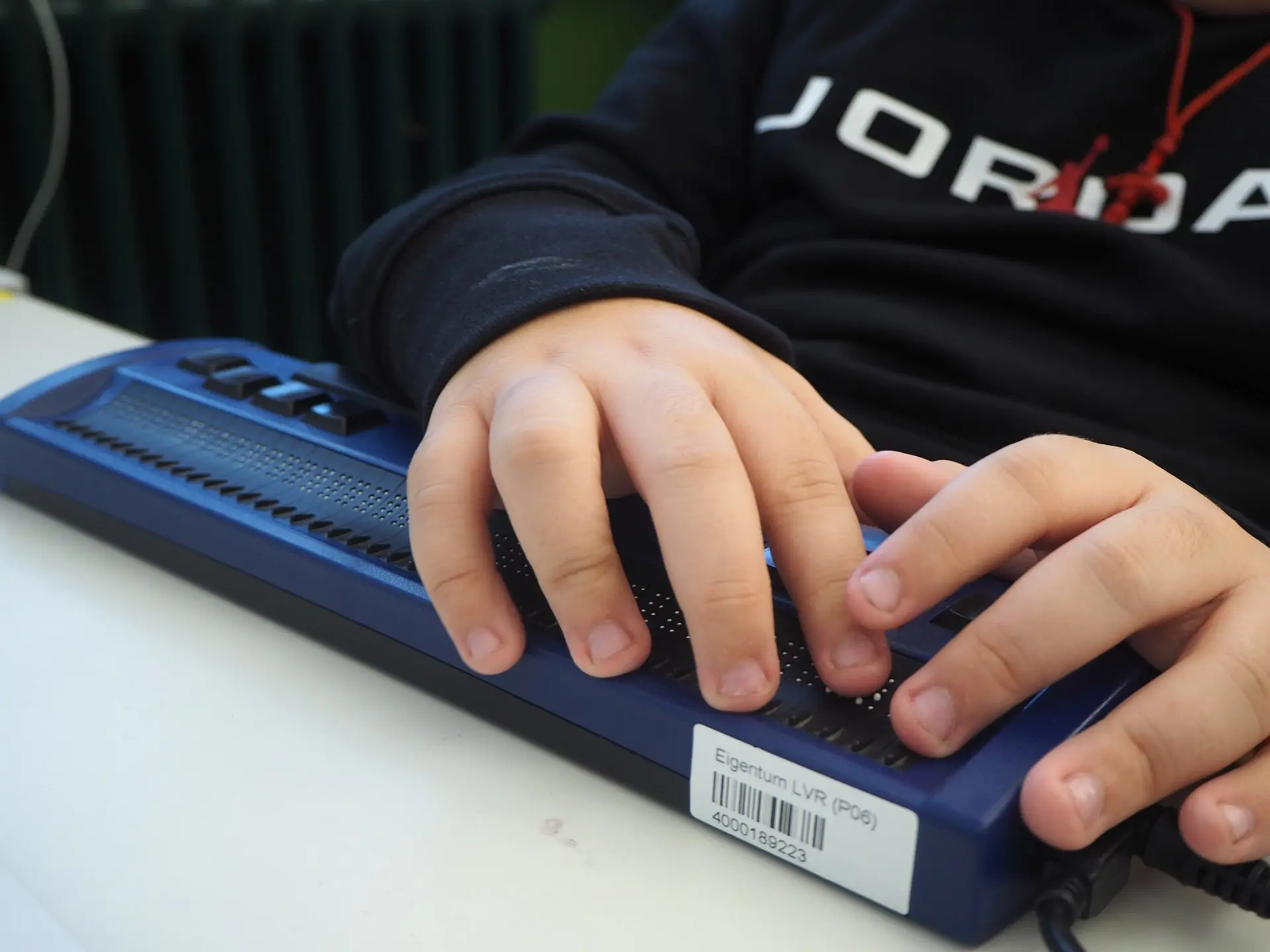 Nahaufnahme der Hände eines Kindes beim Lesen auf einer Braillezeile, die zur taktilen Ausgabe digitaler Texte dient.